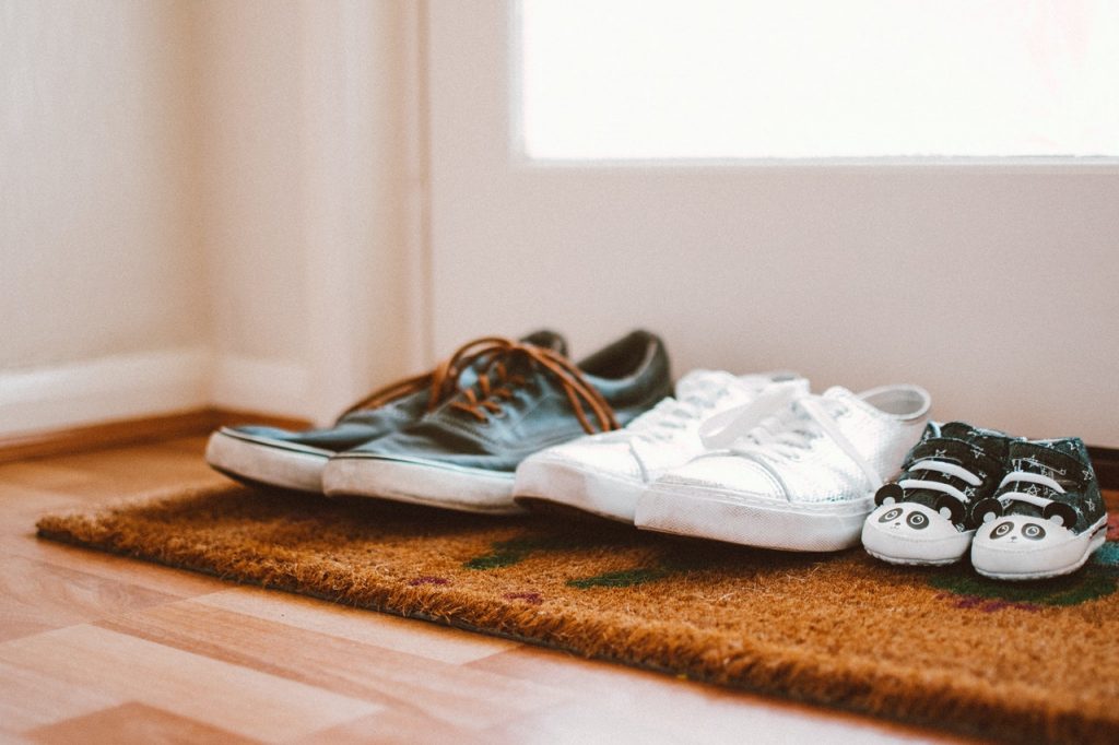 trois paires de chaussures posées sur tapis à l'entrée d'un logement